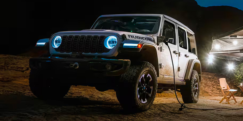 A grey 2025 Jeep Wrangler 4xe parked and charging at night.