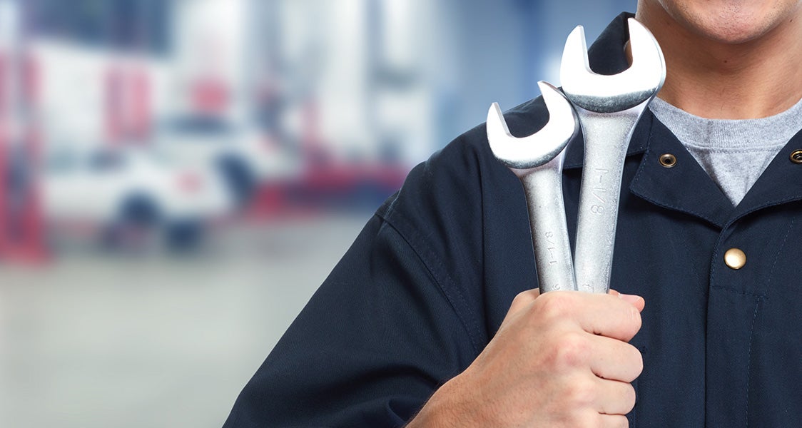 Auto mechanic holding two wrenches in an automotive service center.